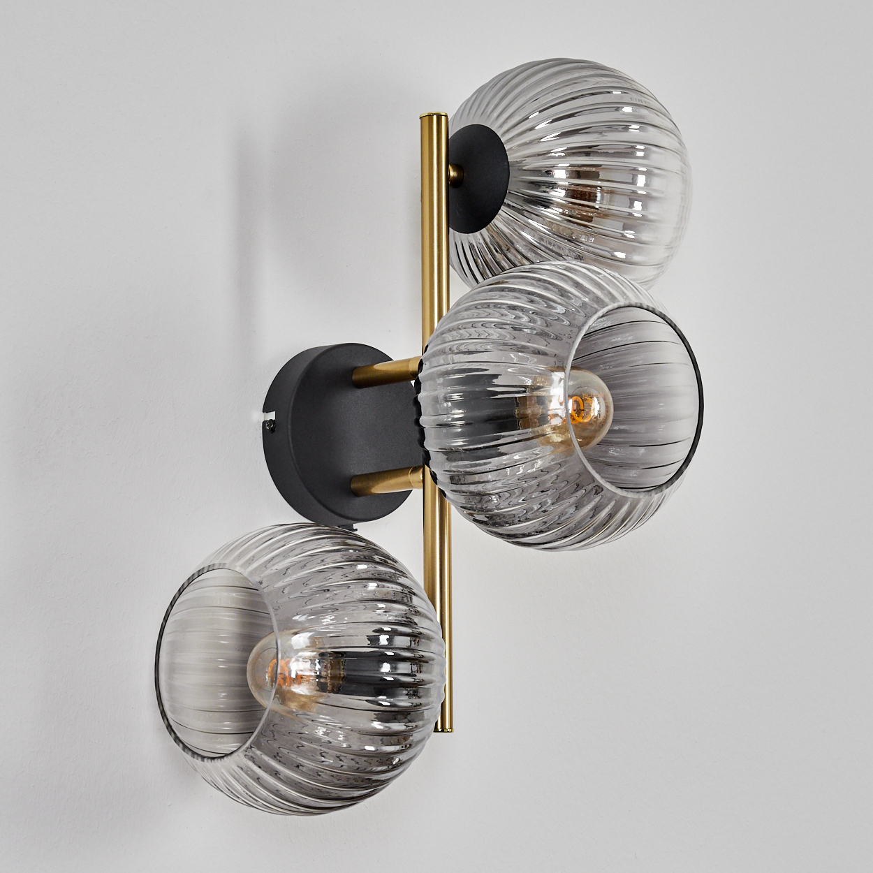 Eine moderne Wandlampe mit drei Glaskugeln. Jede Kugel hat eine Glühbirne. Die Lampe ist an einer weißen Wand befestigt.