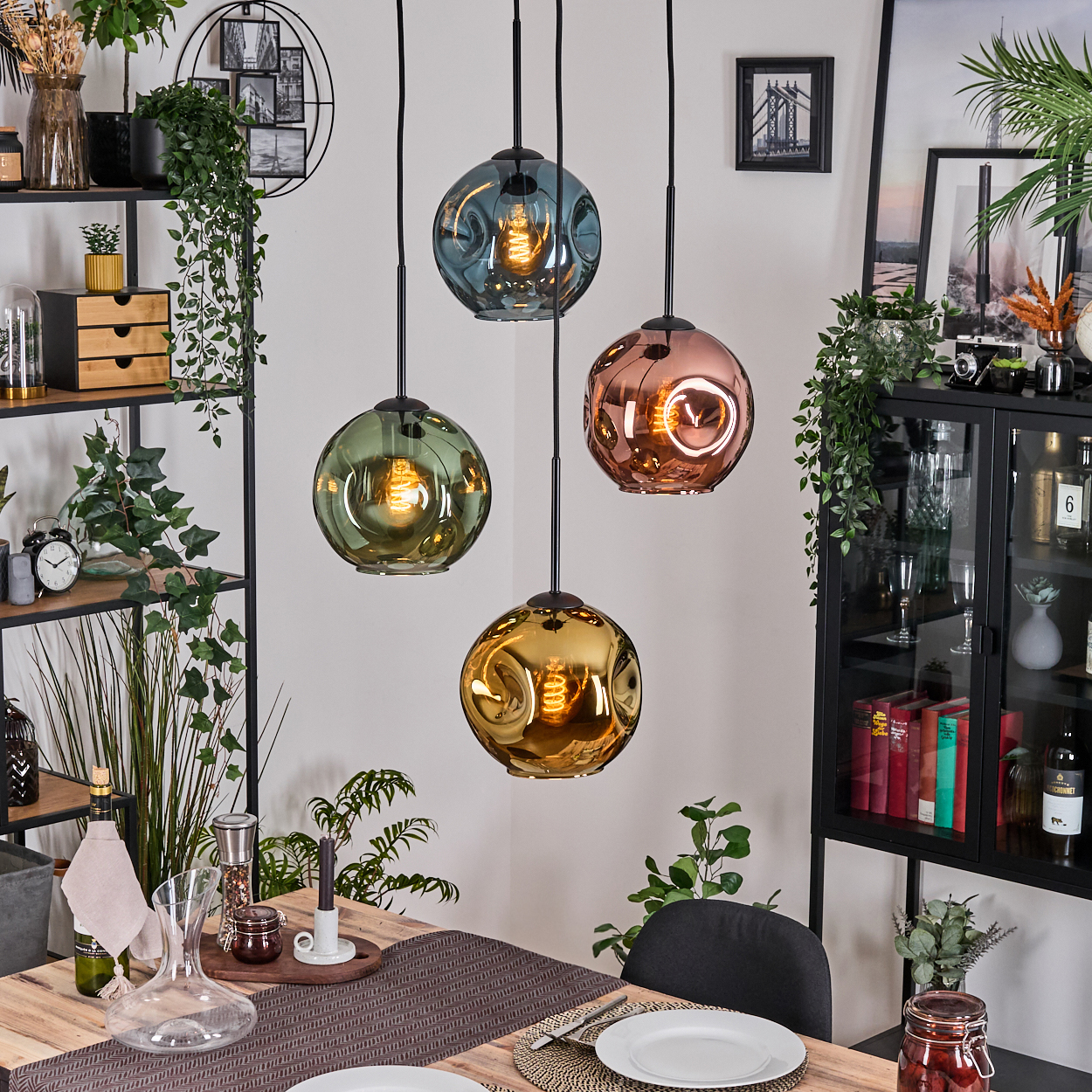 Esszimmer mit vier bunten Glas-Pendelleuchten. Ein Holztisch ist mit Tellern und Dekoration gedeckt. Regale und ein Schrank sind sichtbar.