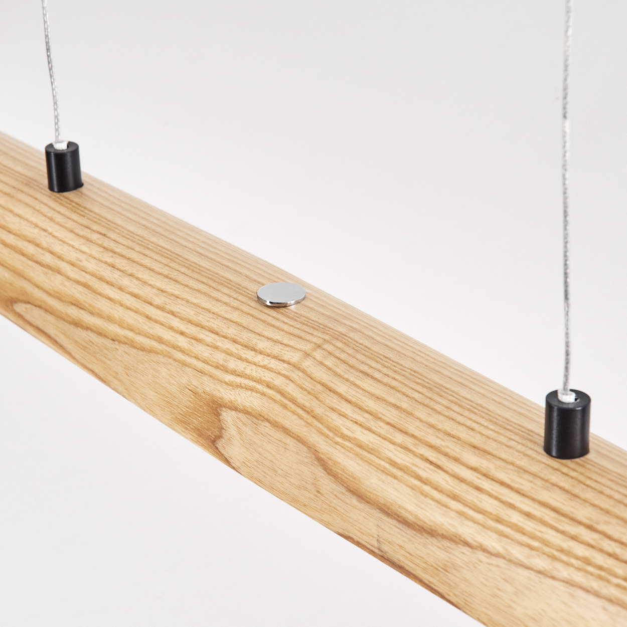 Nahaufnahme eines Holzbalkens mit zwei schwarzen Zylindern an Drähten und einer Metallscheibe. Der Hintergrund ist weiß.