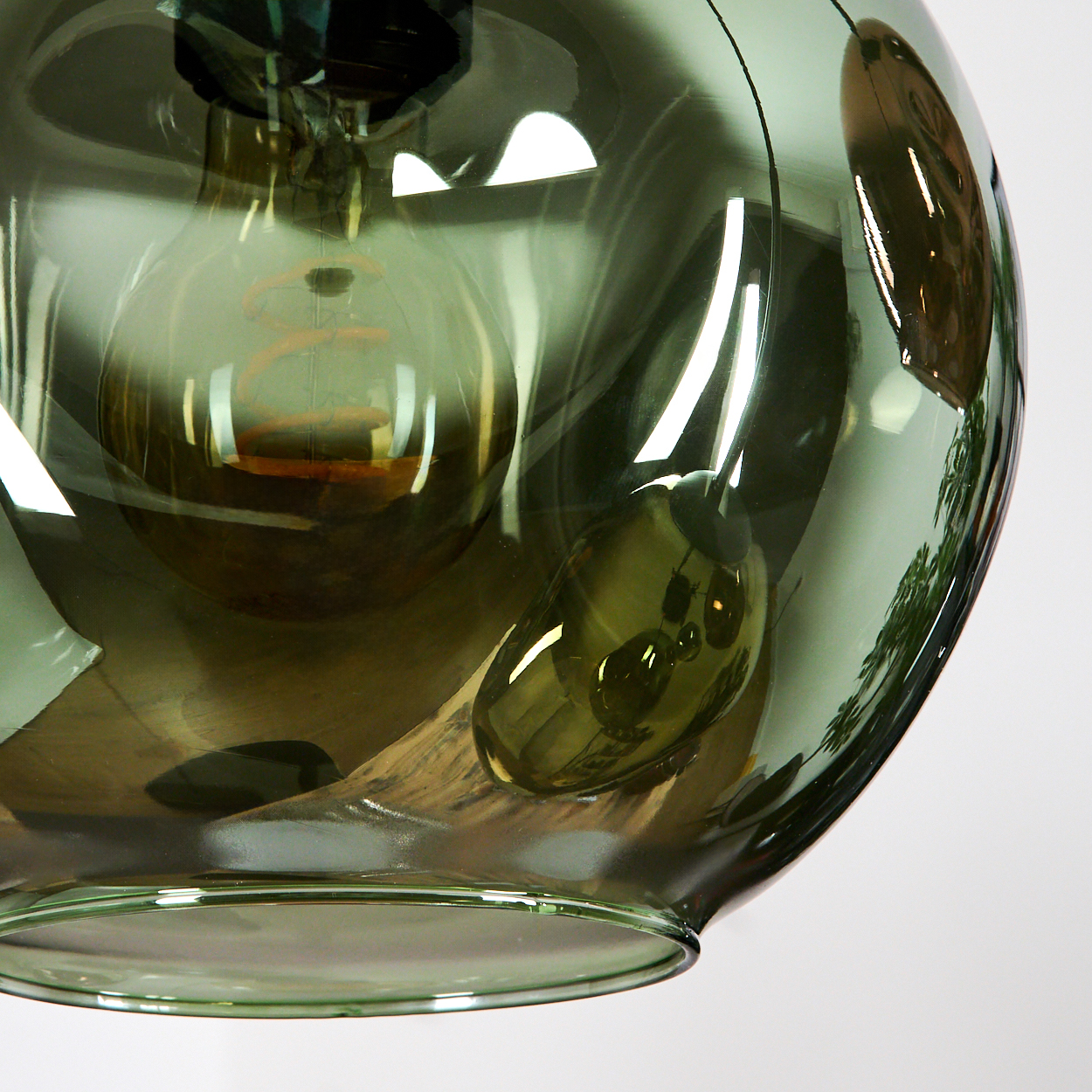 Nahaufnahme einer grünen Glas-Pendelleuchte mit sichtbarer Glühbirne. Reflexionen und Schatten sind im Glas sichtbar.