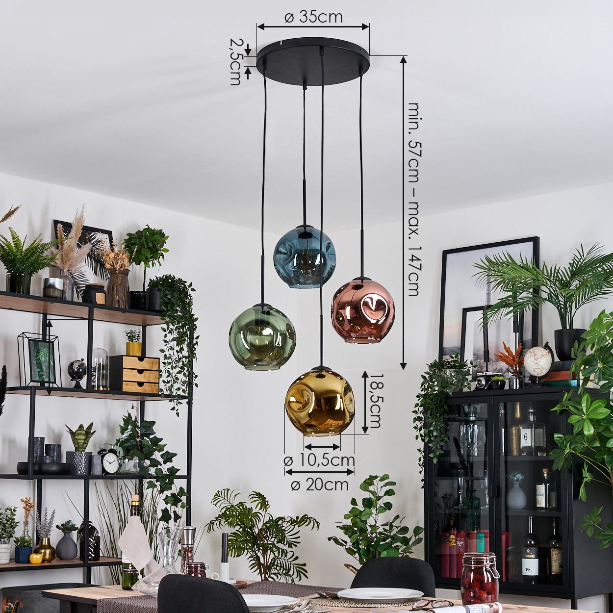 Vier bunte Glas-Pendelleuchten hängen von der Decke. Im Vordergrund ein Esstisch, im Hintergrund Regale und Pflanzen.