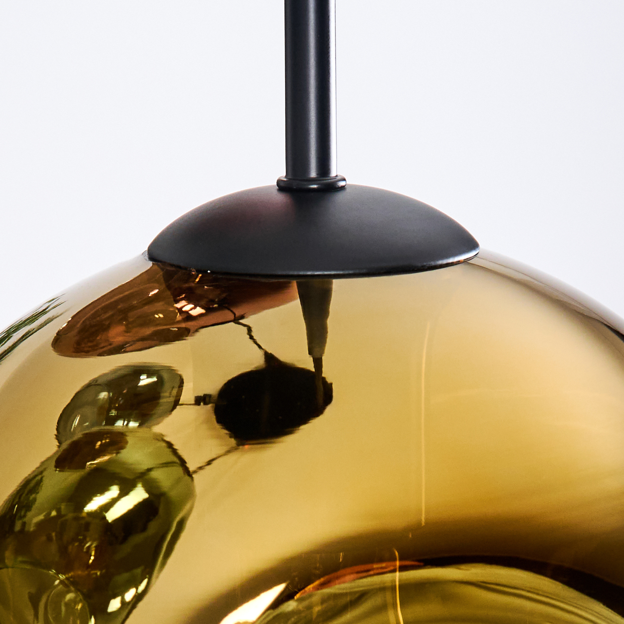 Nahaufnahme einer modernen, goldfarbenen Glas-Pendelleuchte. Sie hat einen schwarzen Metallschaft und eine reflektierende Oberfläche.