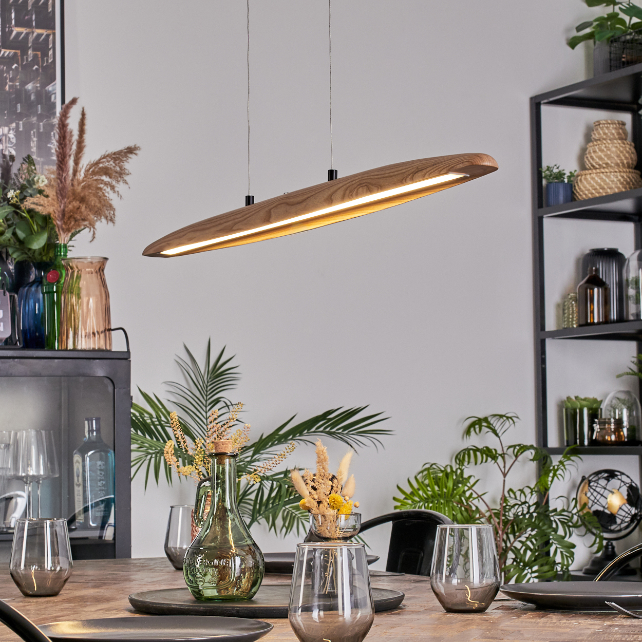 Ein modernes Esszimmer mit einer Holzlampe, einem gedeckten Tisch und Pflanzen im Hintergrund.