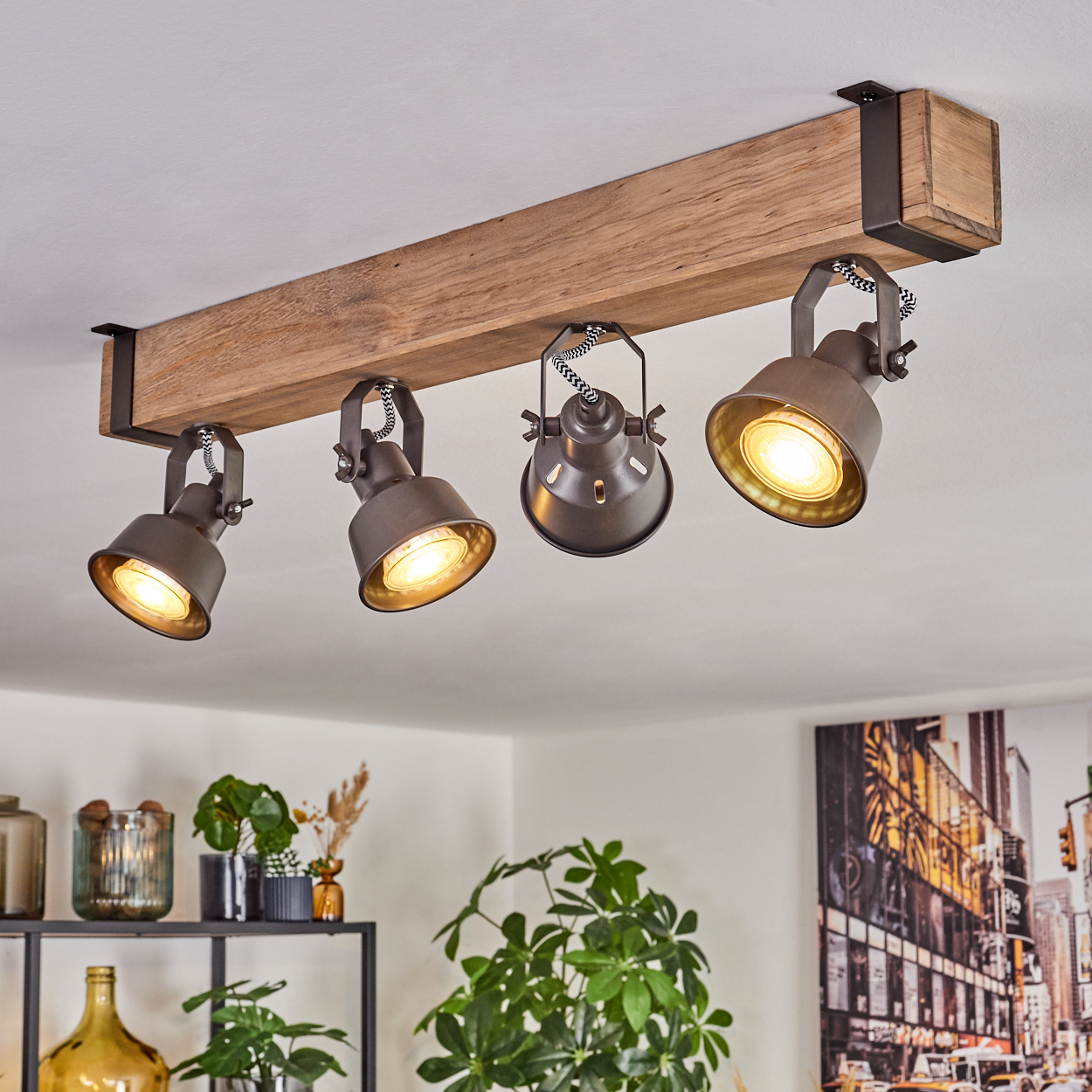 Ein Holzbalken mit vier Strahlern beleuchtet einen Raum. Pflanzen und Dekorationsartikel befinden sich im Vordergrund, ein Stadtbild im Hintergrund.