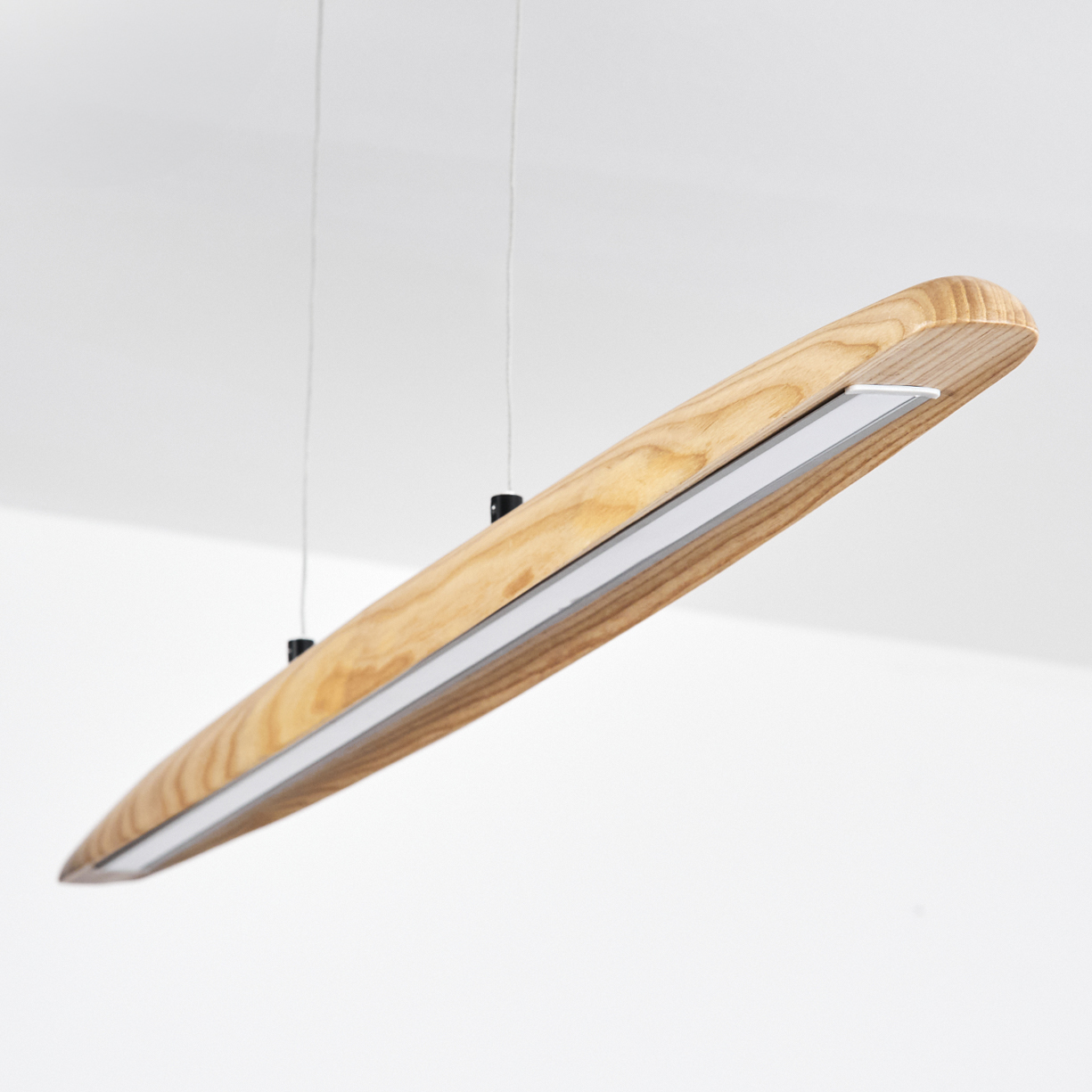 Eine moderne Holz-Pendelleuchte hängt von der Decke. Sie hat einen Lichtstreifen und wird von dünnen Kabeln gehalten.