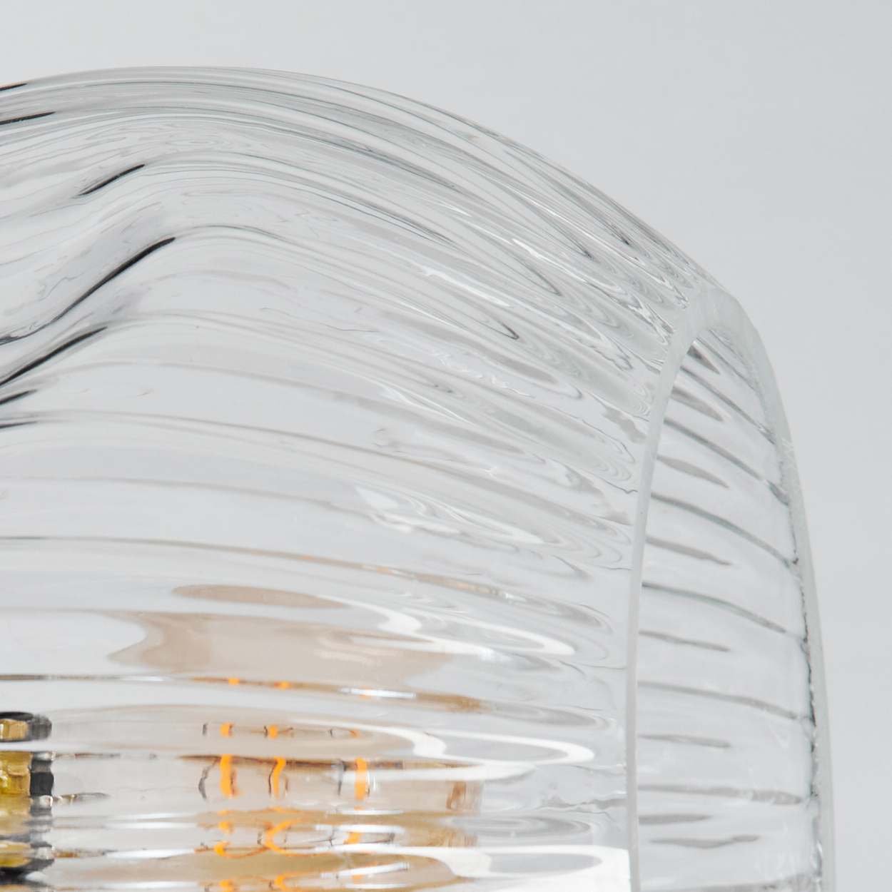 Nahaufnahme eines Lampenschirms aus klarem Glas mit gewellter Struktur. Im Inneren des Glases ist eine orangefarbene Glühbirne zu sehen.