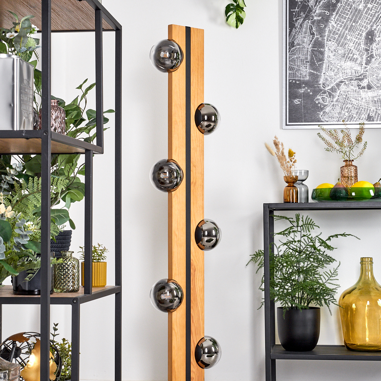 Ein modernes Interieur mit einer Holzlampe mit Glaskugeln. Regale mit Pflanzen, Vasen und einer Karte an der Wand.
