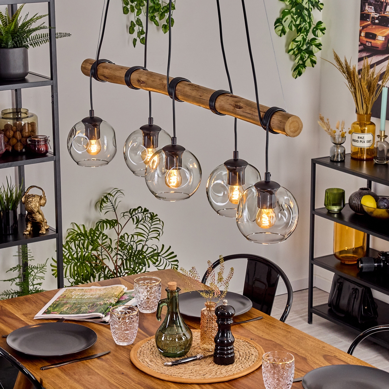 Esszimmer mit Holztisch, Hängelampen und verschiedenen Dekorationen. Enthält Teller, Gläser und eine grüne Flasche.