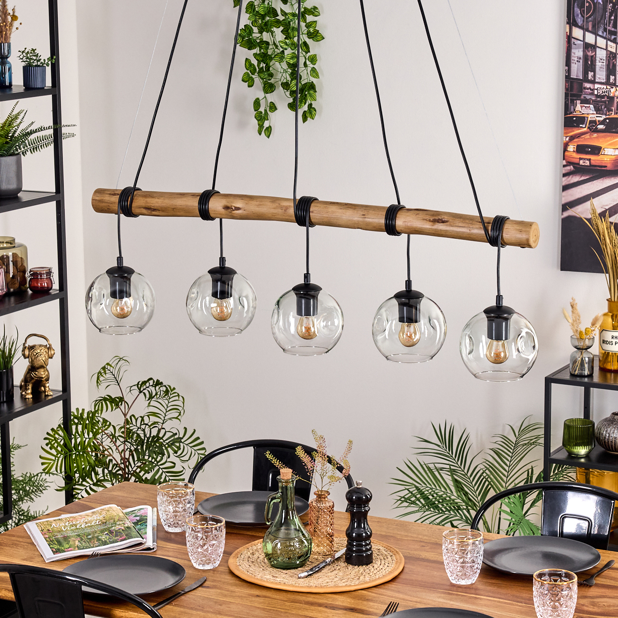 Esszimmer mit Holztisch, schwarzen Stühlen und einzigartiger Leuchte mit Glaskugeln. Pflanzen und Dekoration sind sichtbar.