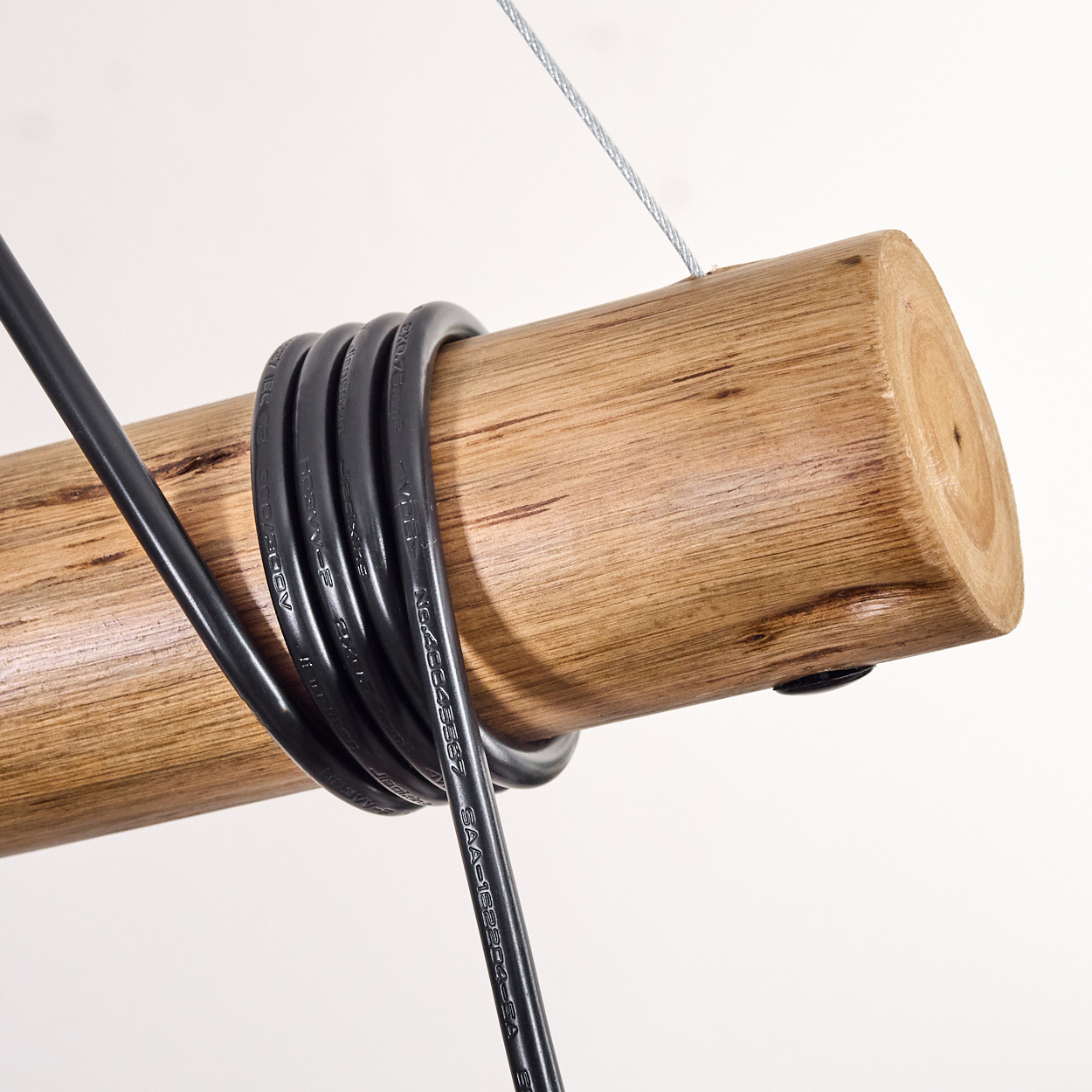 Holzstamm mit schwarzem Kabel, das darum gewickelt ist, an einem Draht aufgehängt, vor weißem Hintergrund. Nahaufnahme.