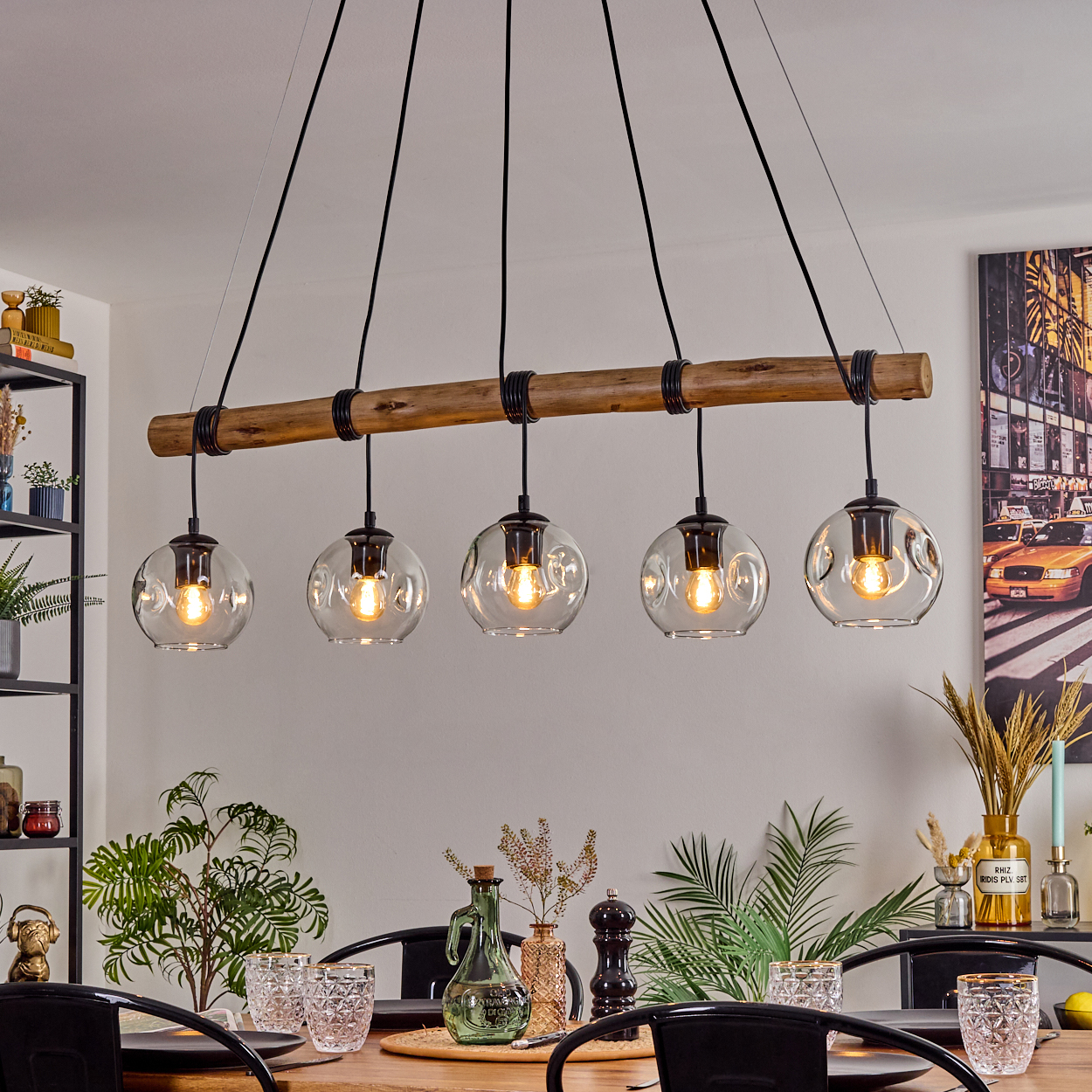 Ein Esszimmer mit Holztisch und schwarzen Stühlen. Darüber trägt ein Holzbalken fünf Glaskugelleuchten.