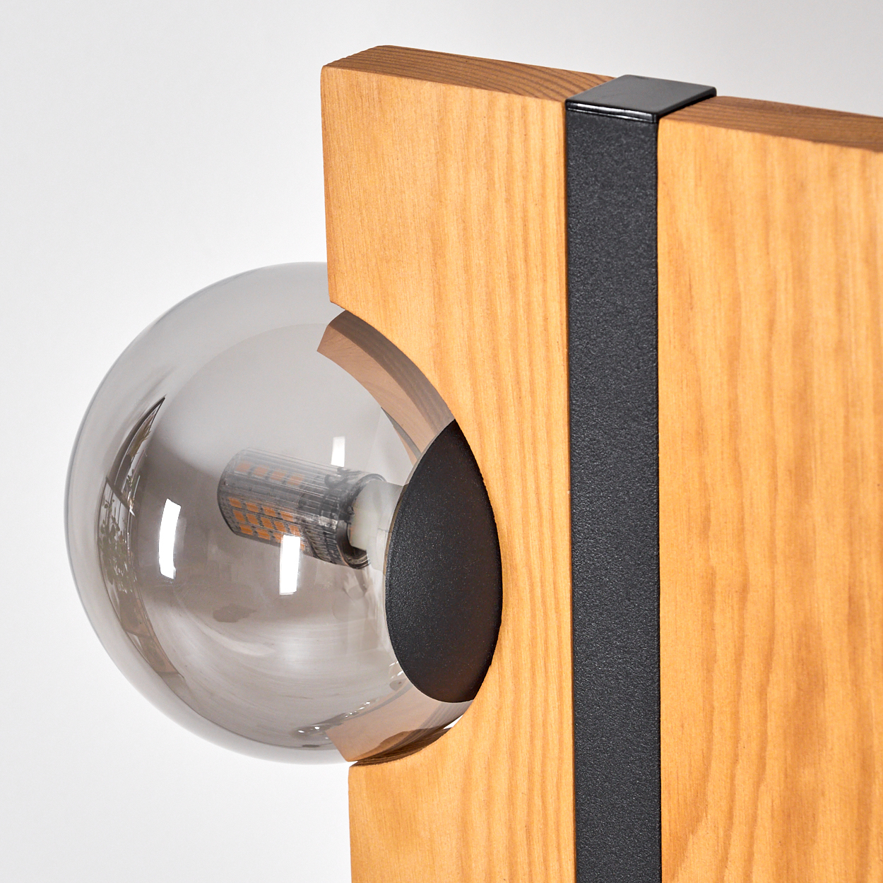 Nahaufnahme einer modernen Lampe. Sie hat eine rauchige Glühbirne, die in einem Holzrahmen mit einem schwarzen Metallstreifen vor weißem Hintergrund sitzt.