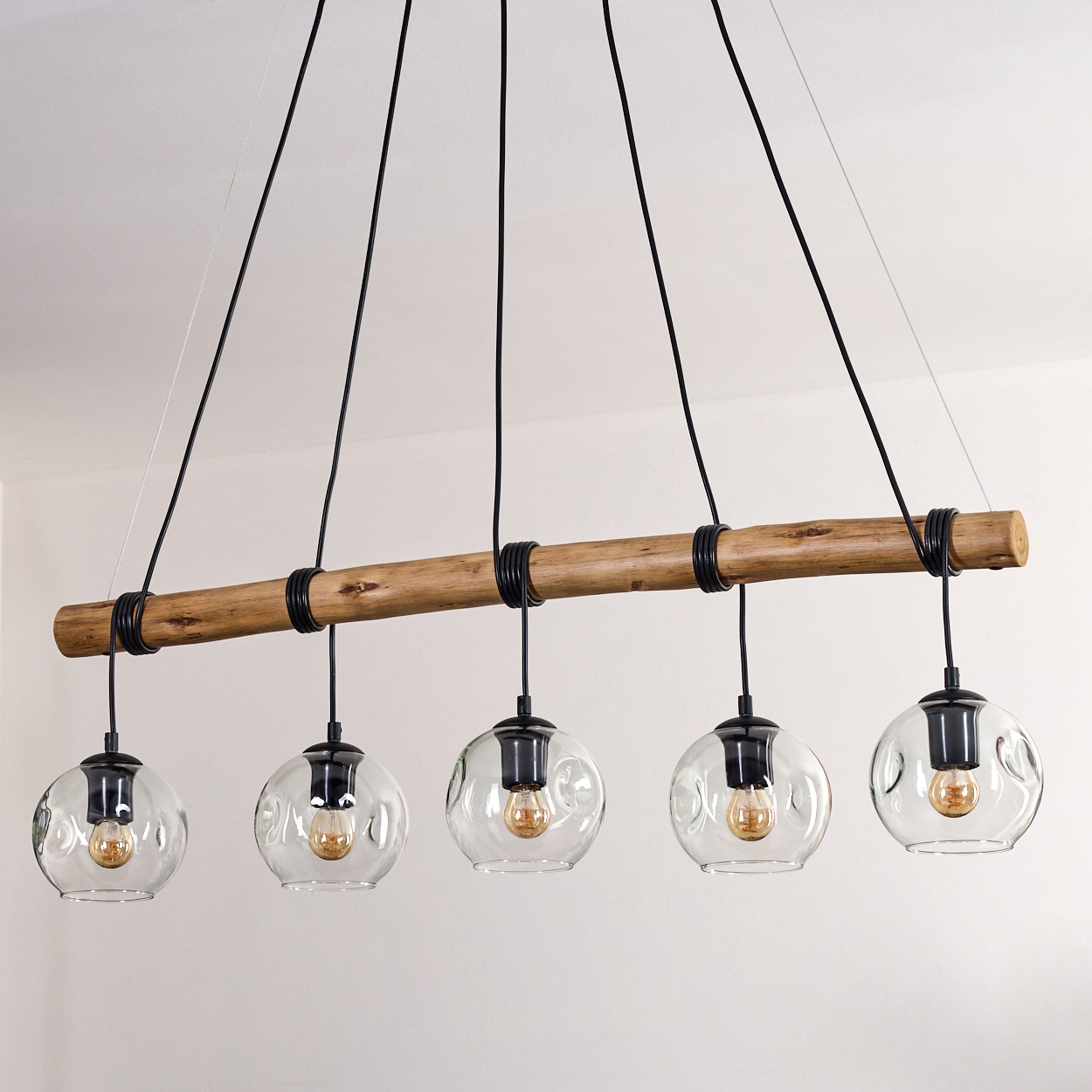 Eine moderne Hängelampe mit fünf Glaskugelleuchten, die an einem Holzbalken hängen. Die Decke ist weiß.