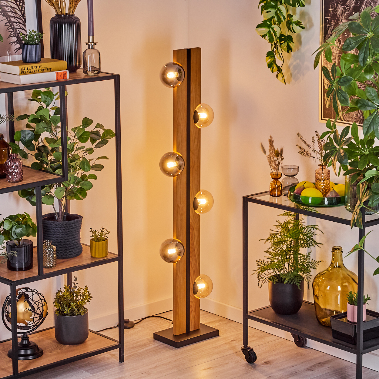 Ein modernes Wohnzimmer mit einer hölzernen Stehlampe, Regalen mit Pflanzen und einem kleinen Rollwagen mit Dekoration.
