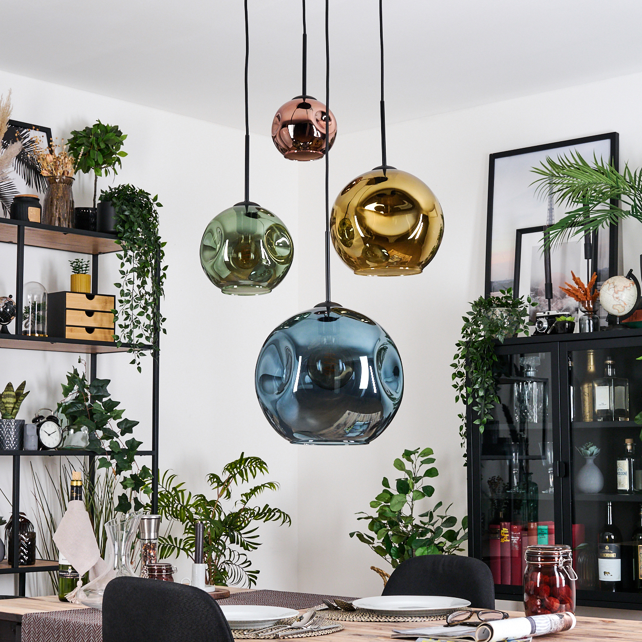 Esszimmer mit vier kugelförmigen Hängelampen. Pflanzen und Regale mit Dekorationsartikeln sind im Hintergrund sichtbar.