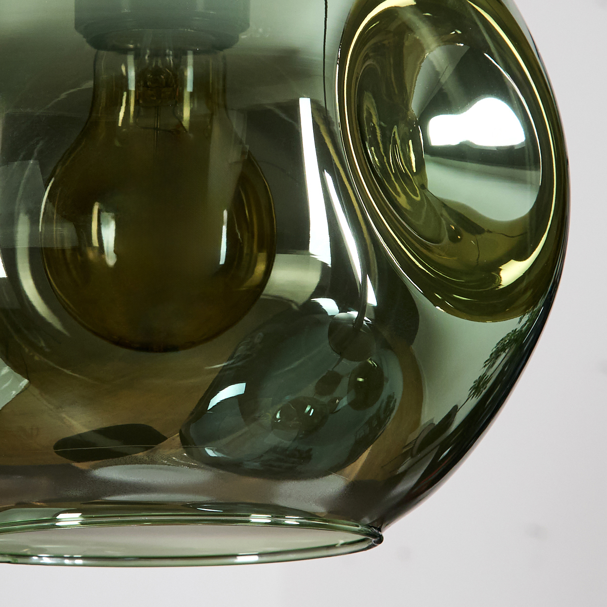 Nahaufnahme einer grünen Glaslampe mit einer Glühbirne. Die Lampe hat eine einzigartige, abstrakte Form mit Reflexionen.