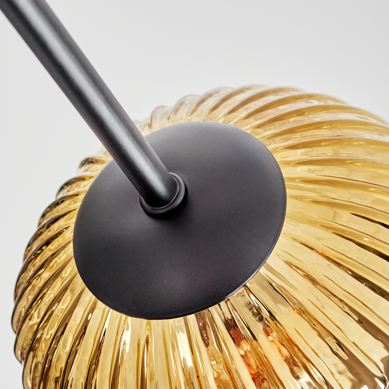 Nahaufnahme einer Lampe. Mit einem schwarzen Arm und einer kreisförmigen schwarzen Basis, die einen goldfarbenen, gerippten Glasschirm hält.