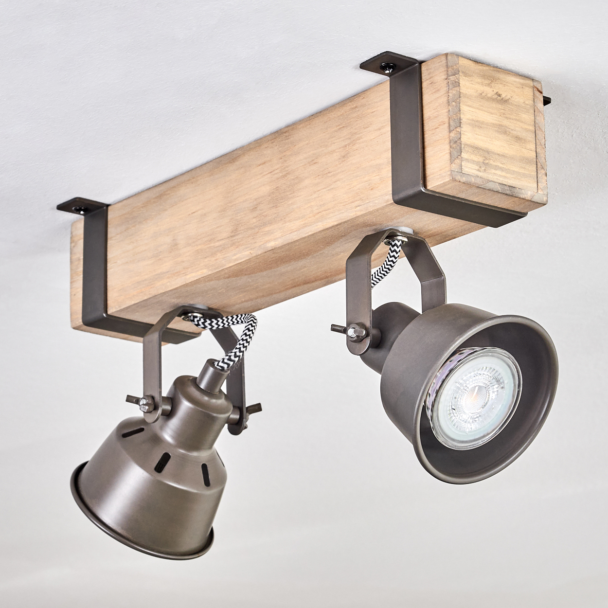 Eine Deckenleuchte mit Holzbalken und zwei Metall-Spots. Die Leuchten haben ein schwarz-weiß gestreiftes Kabel.