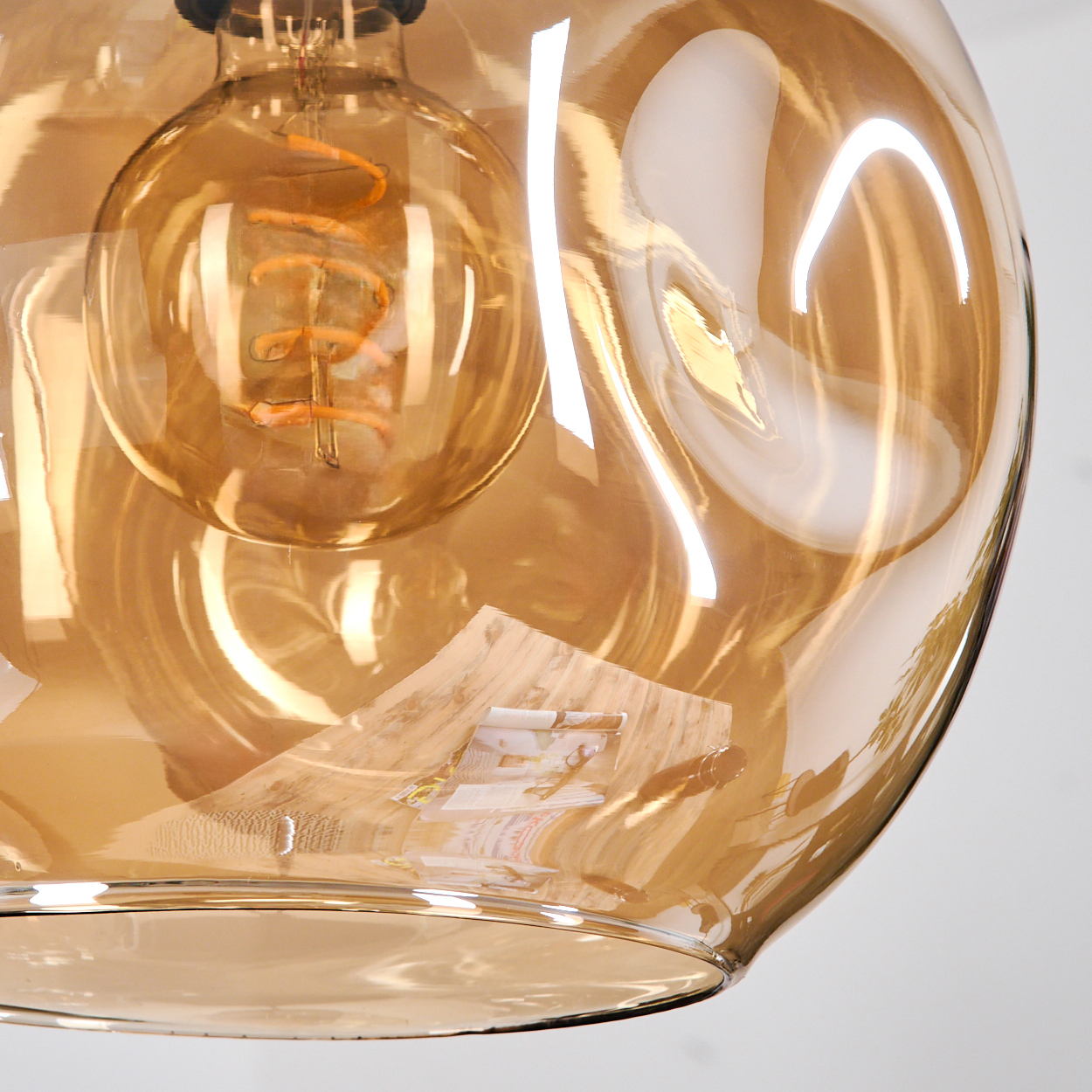 Nahaufnahme einer Glasleuchte mit Glühbirne. Das Glas ist bernsteinfarben und reflektiert Licht. Ein Papier ist im Glas sichtbar.