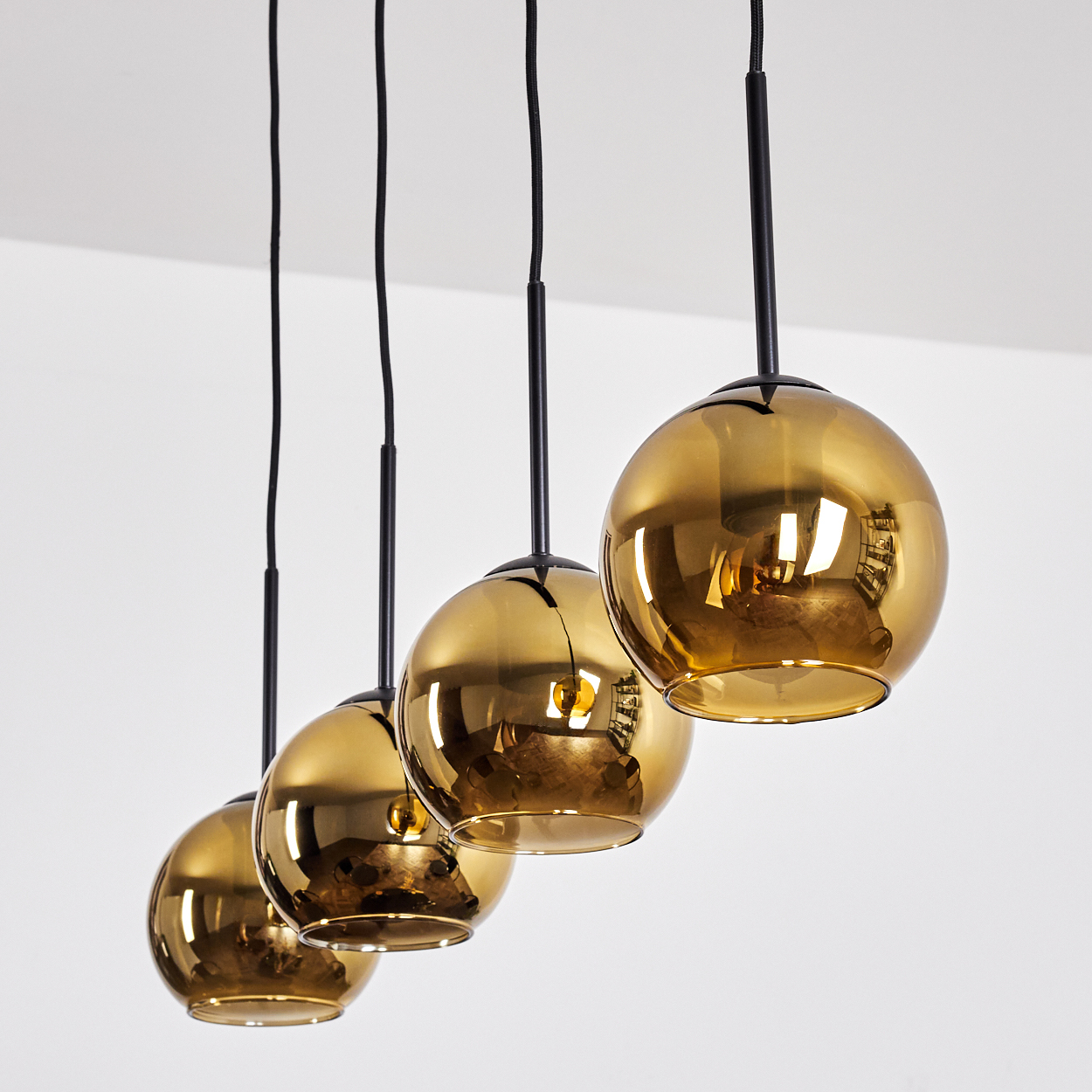 Vier goldene Pendelleuchten hängen von der Decke. Jede hat einen kugelförmigen Schirm und ein schwarzes Kabel. Weißer Hintergrund.
