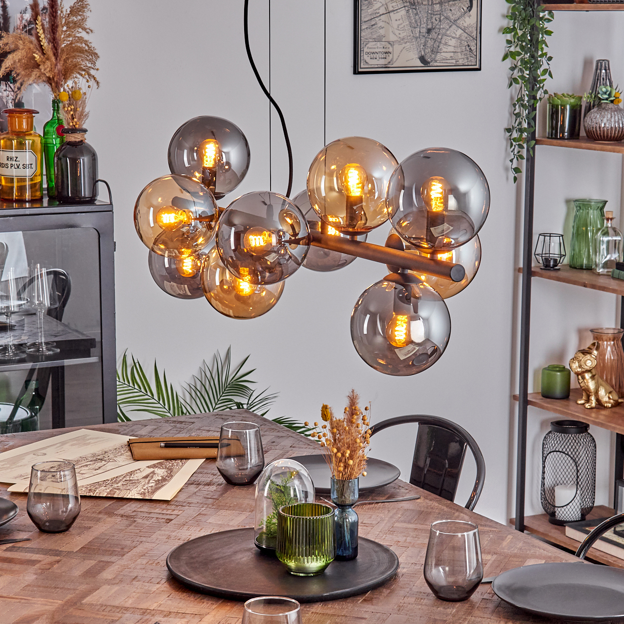 Ein Esszimmer mit Holztisch, modernem Kronleuchter, Gläsern und Deko. Im Hintergrund Regale und ein schwarzer Schrank.