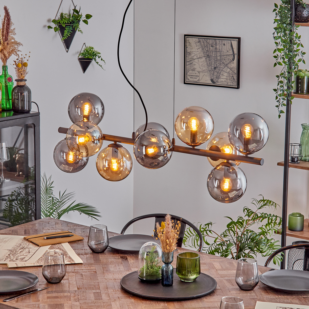 Ein Esszimmer mit einem Holztisch, der zum Abendessen gedeckt ist. Eine moderne Deckenleuchte hängt darüber. Pflanzen und Dekoration sind im Raum angeordnet.