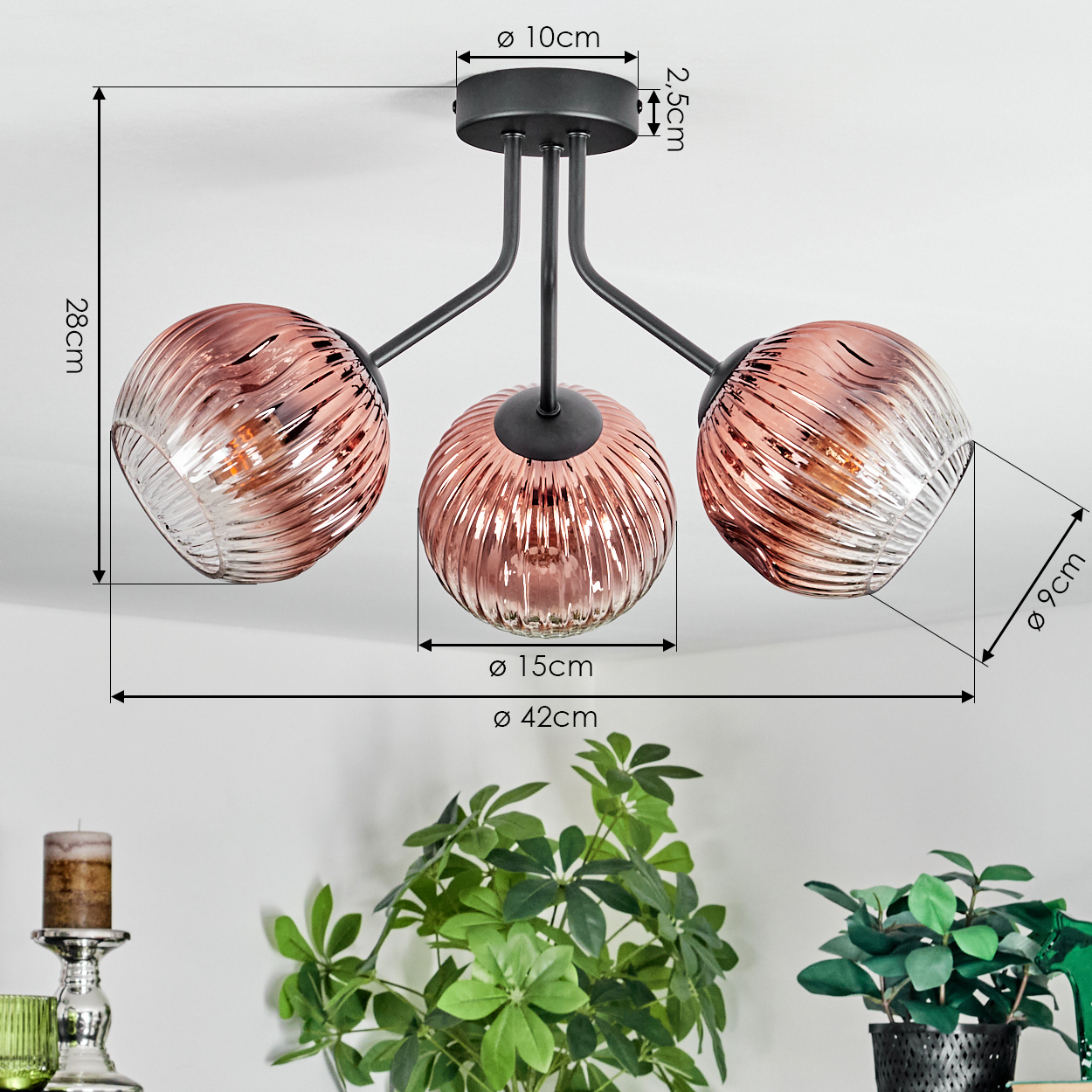 Moderne Deckenlampe mit drei rosafarbenen Glaskugeln. Maße sind angegeben. Grüne Pflanzen und ein Kerzenhalter sind im Vordergrund.