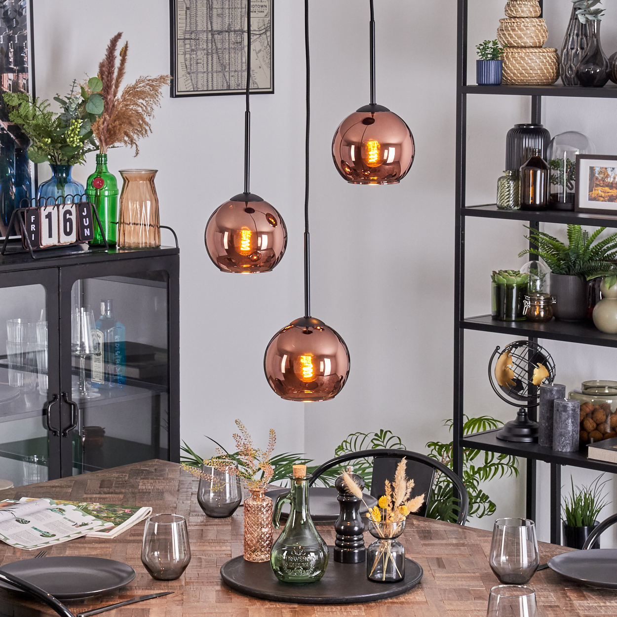 Esszimmer mit Kupfer-Hängelampen, Holztisch für das Abendessen gedeckt. Regale mit Dekoration im Hintergrund.