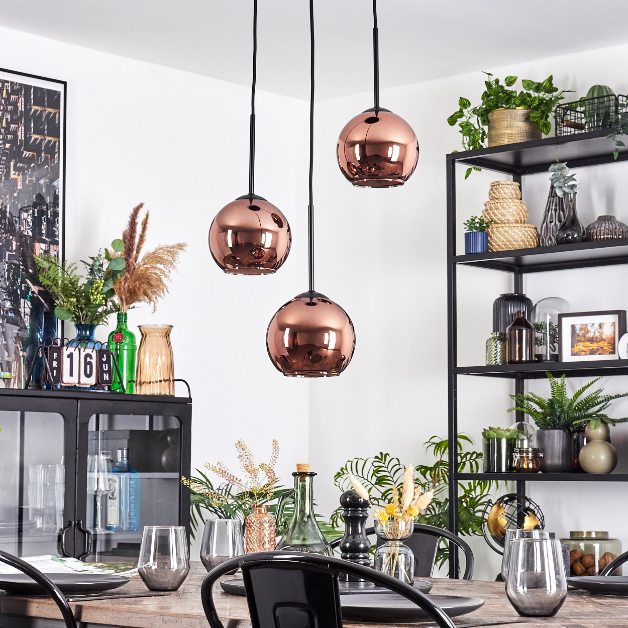 Esszimmer mit kupferfarbenen Pendelleuchten, einem gedeckten Tisch, einem schwarzen Regal mit Pflanzen und einem schwarzen Schrank.