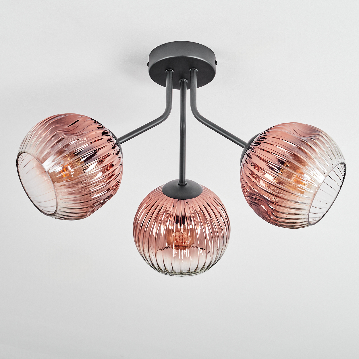 Moderne Deckenlampe mit drei rosa Glaskugeln. Die Lampe befindet sich vor einem weißen Hintergrund.