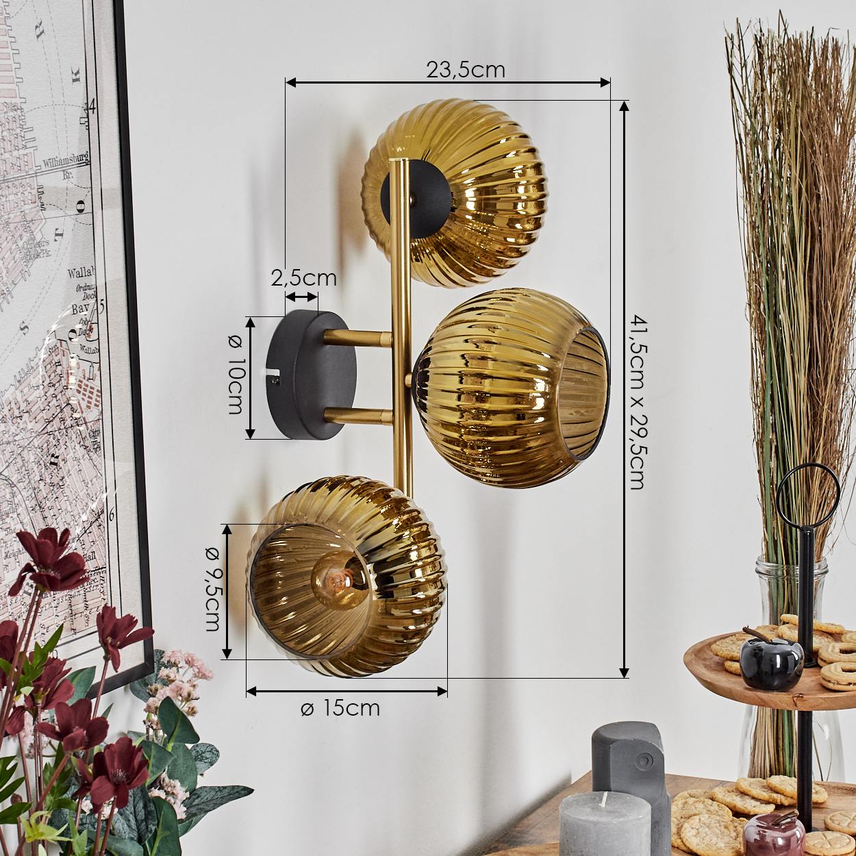 Goldene Wandlampe mit drei kugelförmigen Schirmen. Abmessungen werden angezeigt. Links eine Karte und Blumen, rechts Snacks.