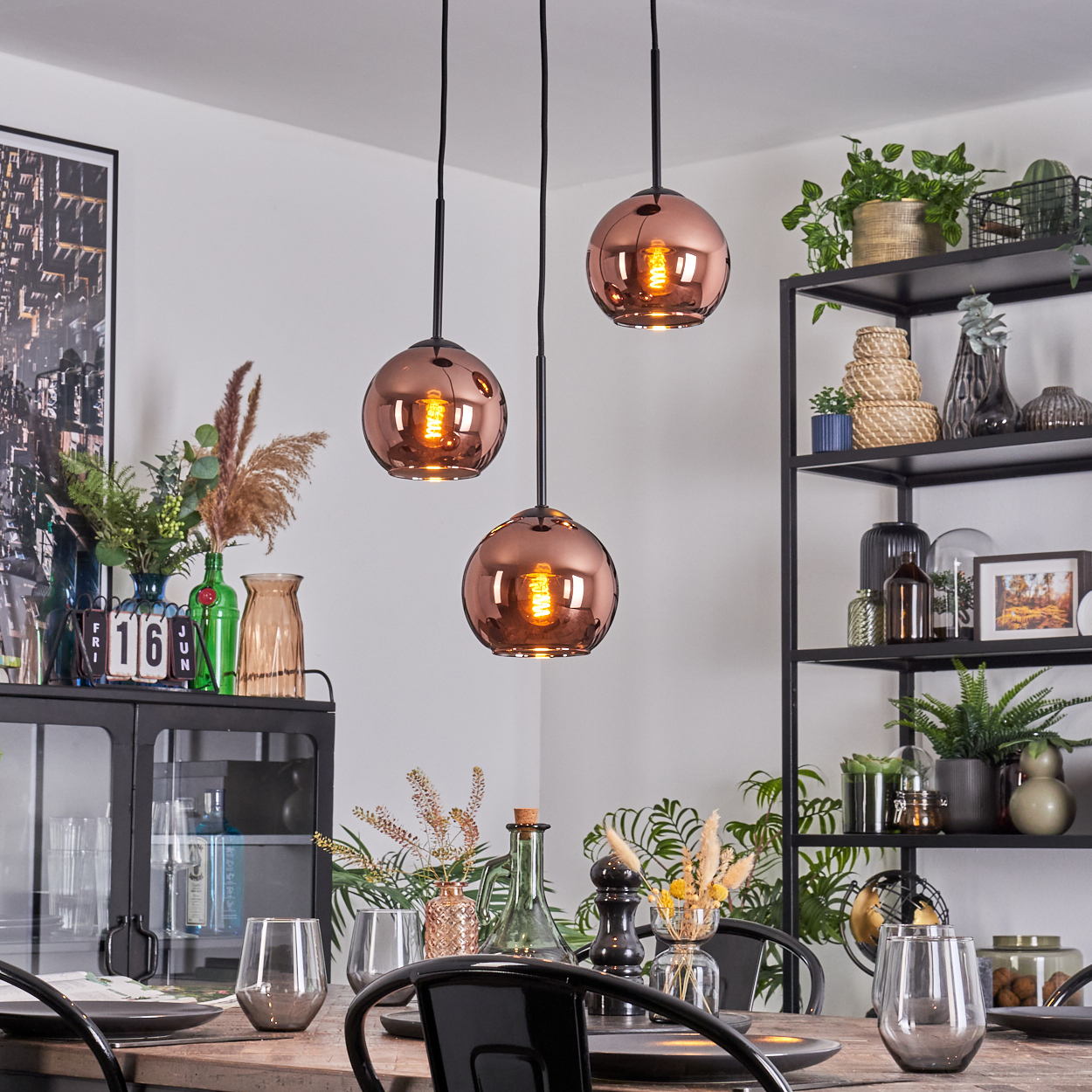 Esszimmer: Kupfer-Pendelleuchten, Holztisch, schwarze Stühle und ein Metallregal mit Pflanzen und Dekoration.