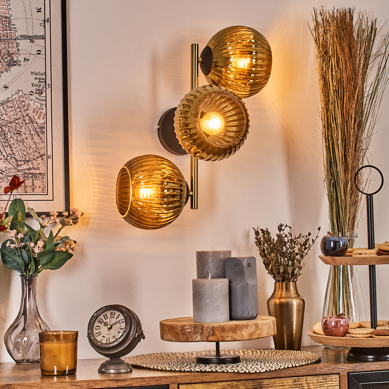 Eine Wandlampe mit drei Glaskugeln. Kerzen, Uhr, Vase mit Blumen und Dekorationsartikel auf einer Holzoberfläche.