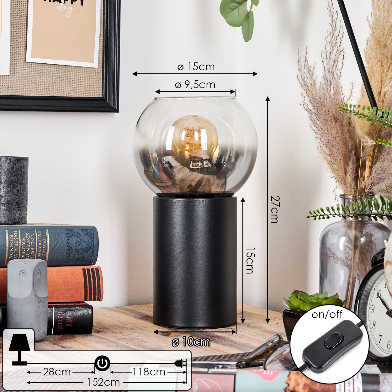 Eine schwarze Lampe mit Glasschirm und sichtbarer Glühbirne steht auf einem Holztisch. Bücher, eine Eulenstatue und ein Ein/Aus-Schalter sind in der Nähe.
