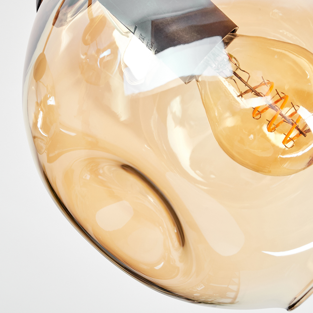 Nahaufnahme einer Leuchte mit Glasschirm und sichtbarer Glühbirne mit Spiralfaden. Der Schirm ist bernsteinfarben.