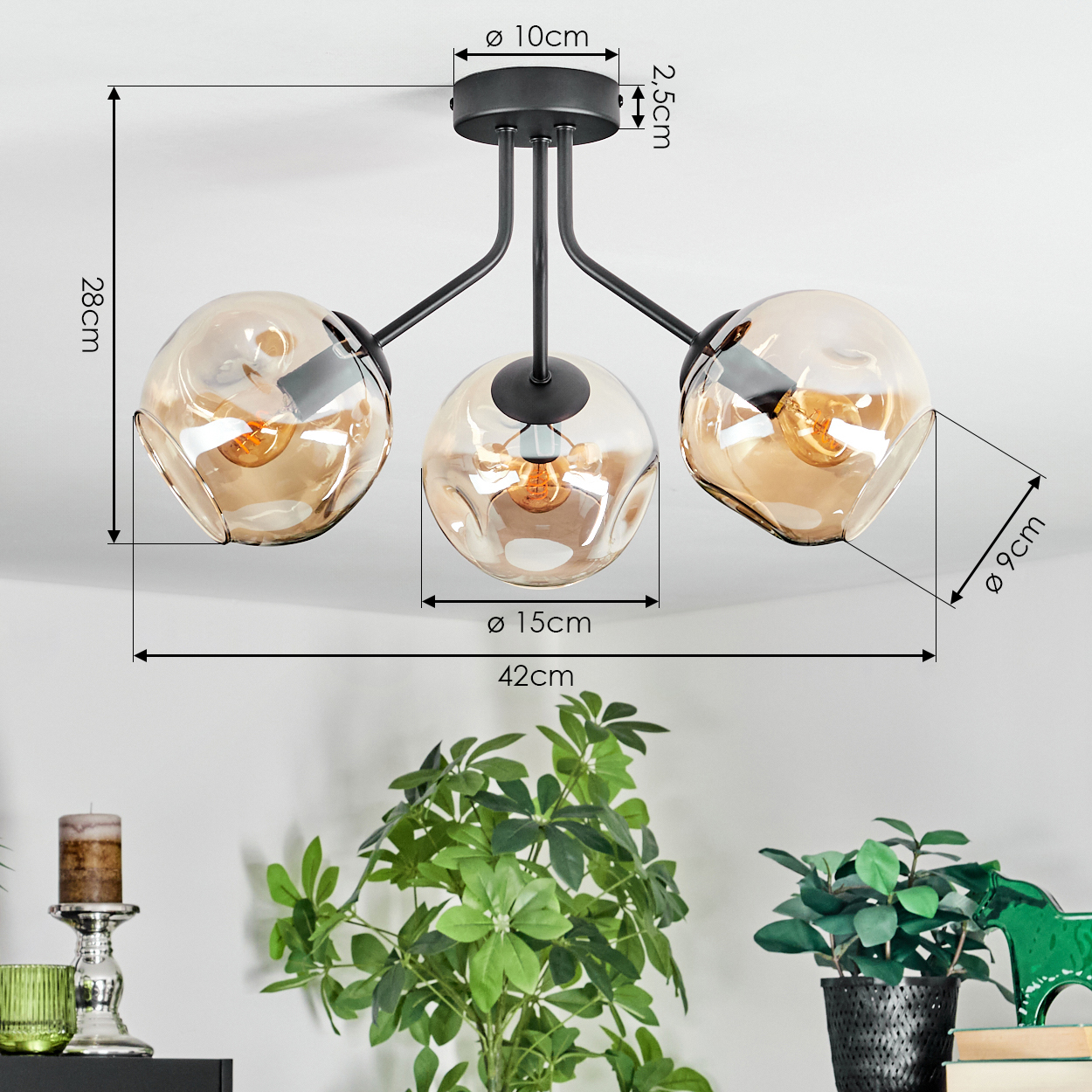 Moderne Deckenlampe mit drei bernsteinfarbenen Glasschirmen. Maße sind angegeben. Pflanzen und Dekoration im Vordergrund.
