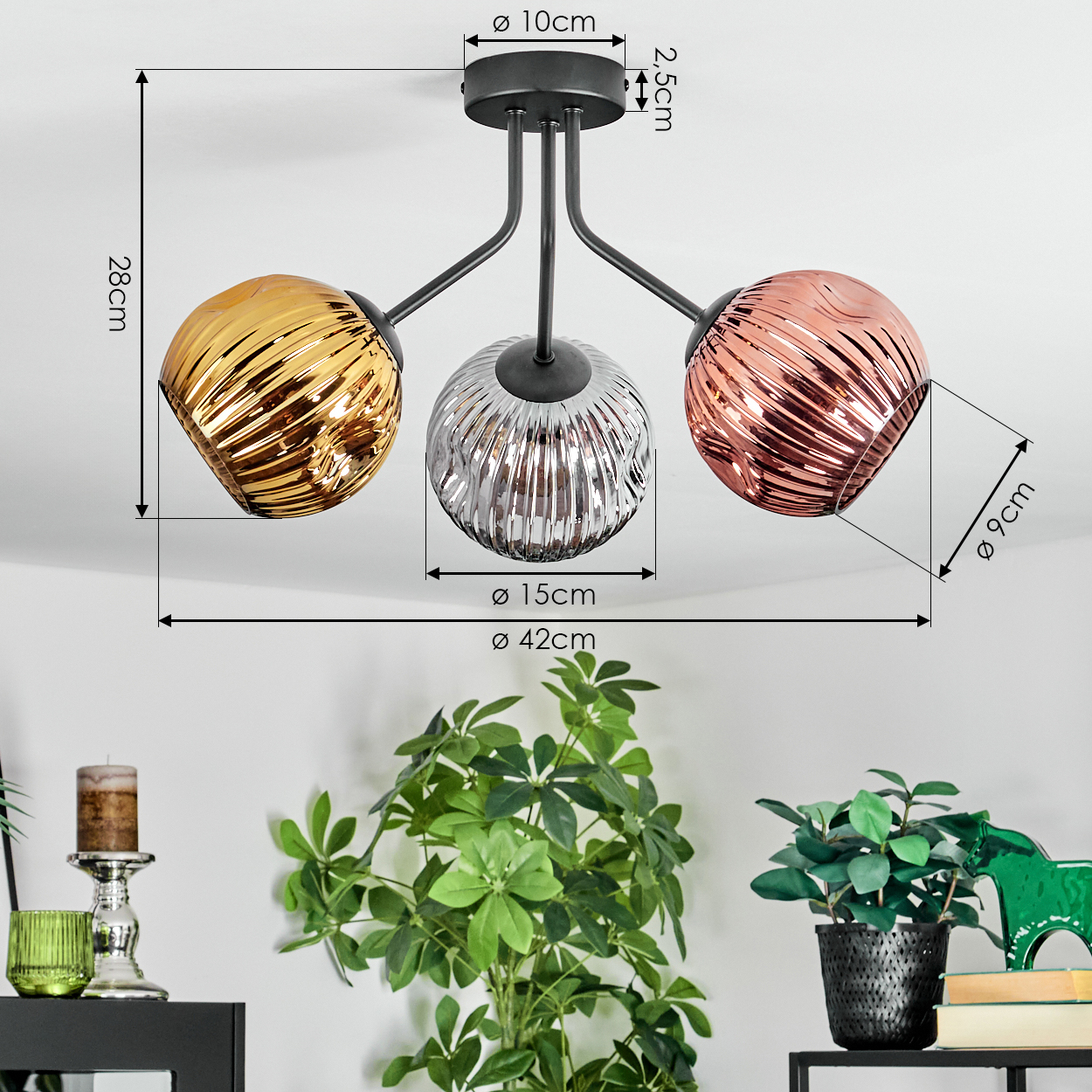 Eine Deckenleuchte mit drei kugelförmigen Schirmen in Gold, Silber und Kupfer. Dekorative Pflanzen und Gegenstände im Vordergrund.