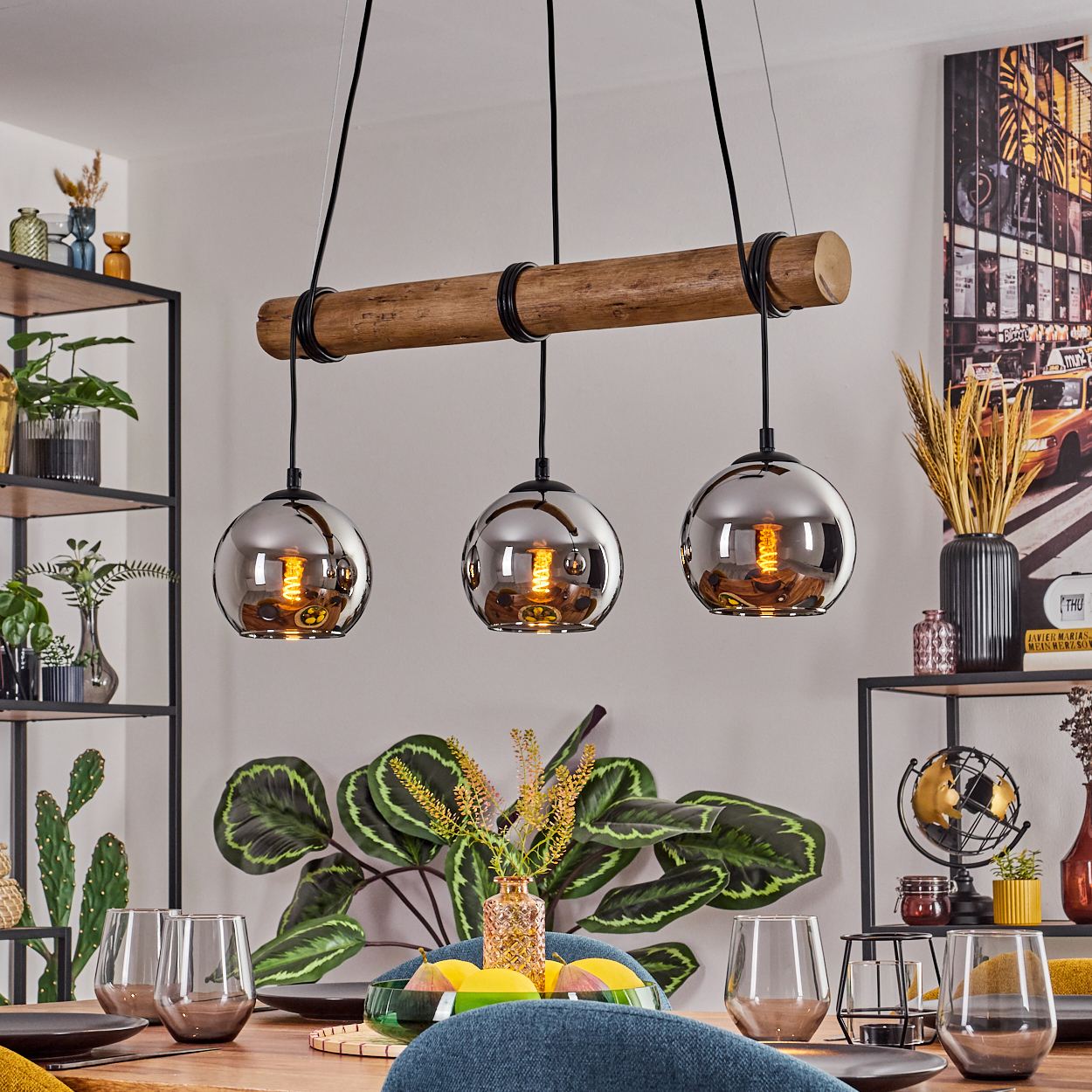 Esszimmer mit Pendelleuchte aus Holzbalken. Glaskugeln hängen über einem Tisch, der mit Gläsern und einer Obstschale gedeckt ist.