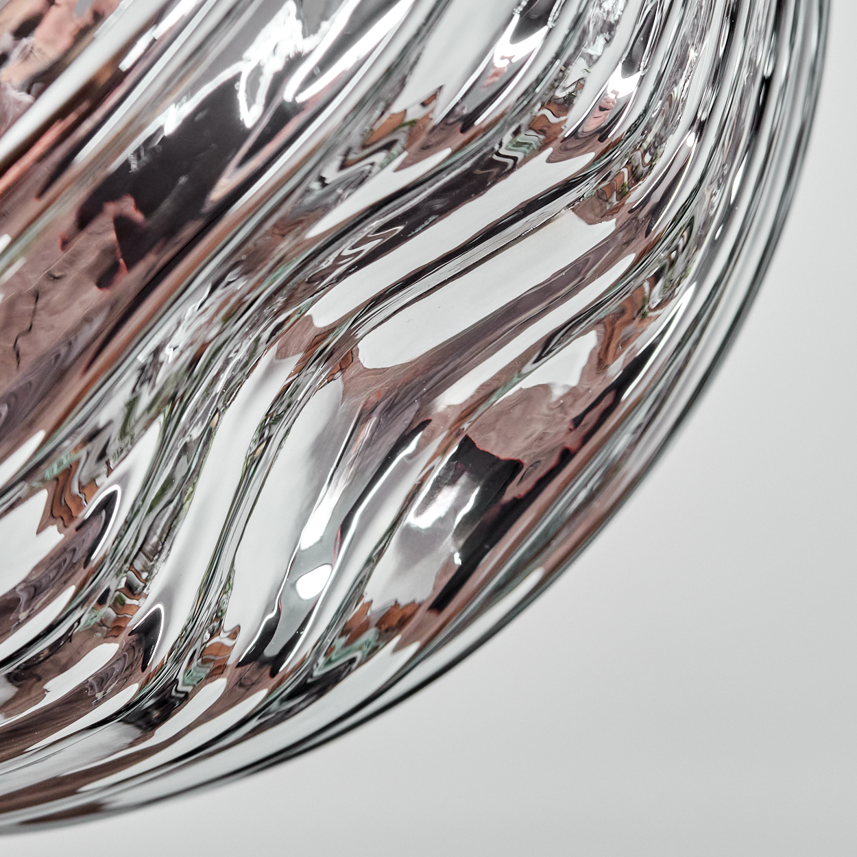 Nahaufnahme eines Glasobjekts mit wellenartigen Mustern, die das Licht reflektieren. Der Hintergrund ist eine weiße Oberfläche.