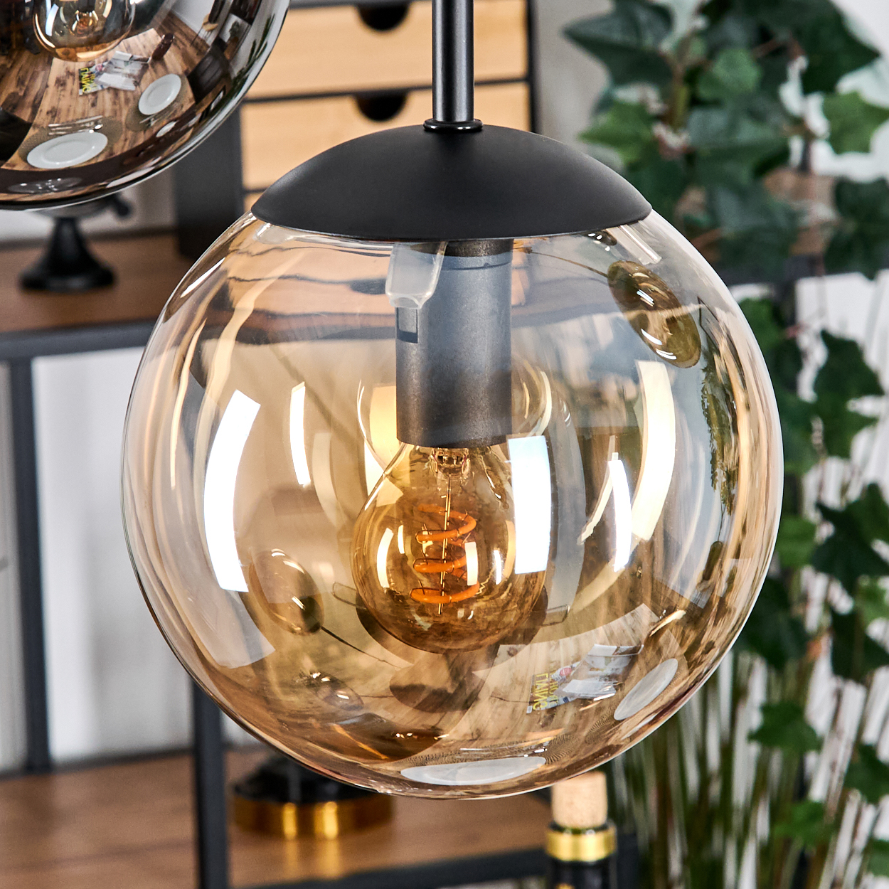 Nahaufnahme einer Pendelleuchte mit Globus-Schirm. Im Inneren des Globus befindet sich eine Glühbirne. Der Hintergrund zeigt Grün und Möbel.