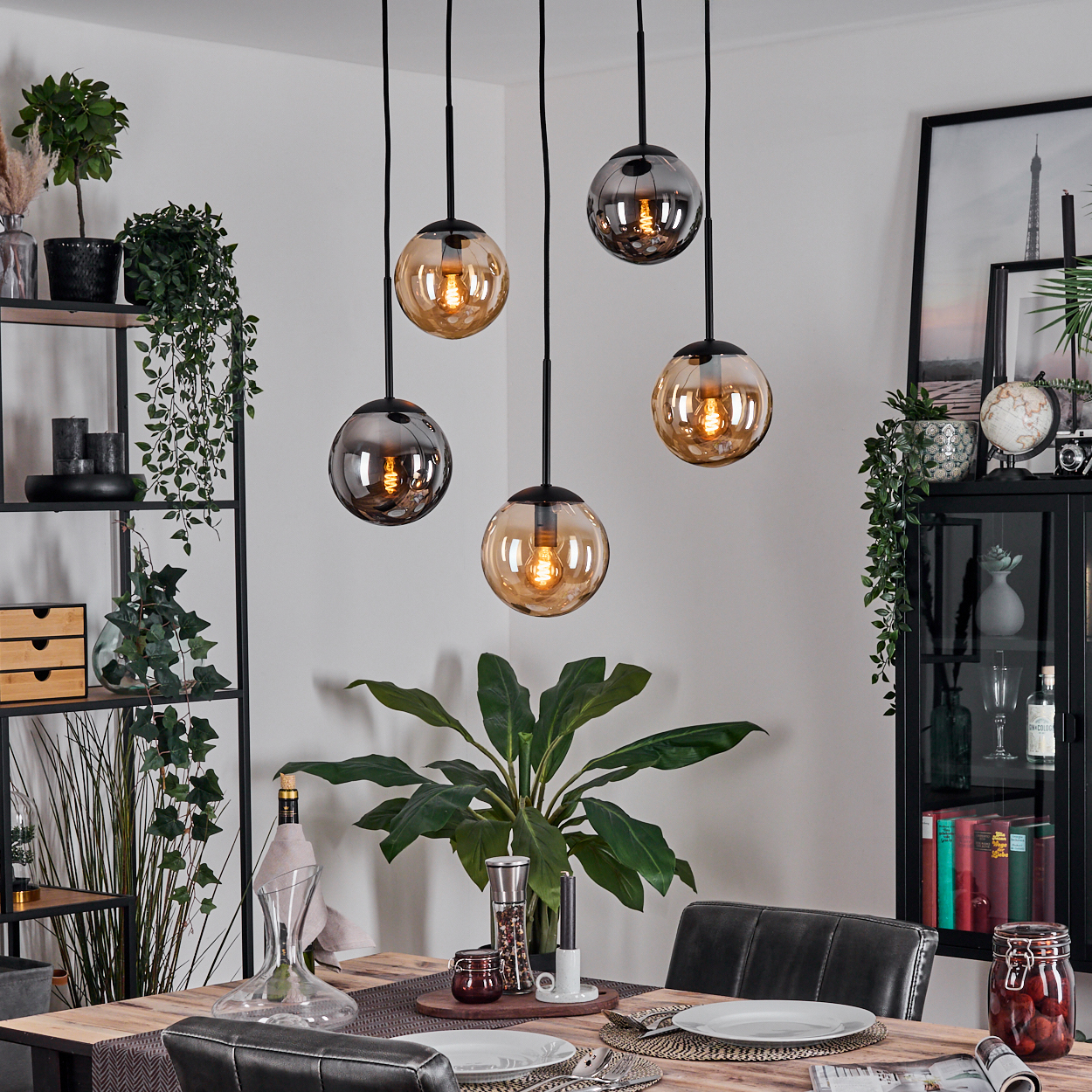Esszimmer mit hängenden Kugelleuchten. Tisch mit Tellern gedeckt. Regale, Pflanzen und Dekoration sind im Hintergrund sichtbar.