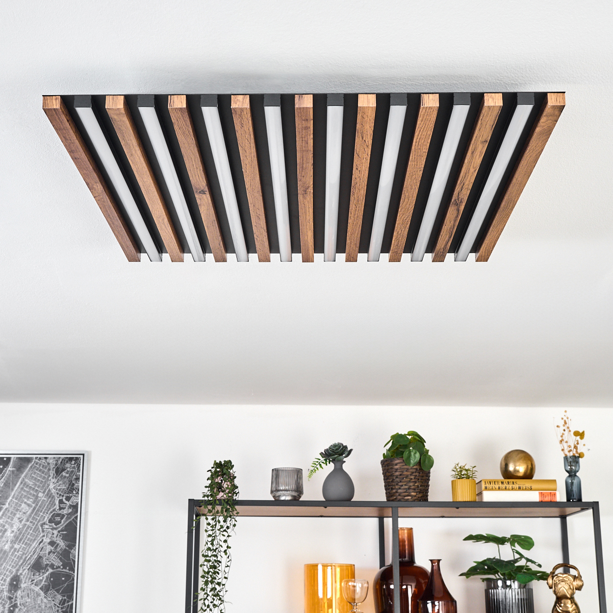 Moderne Deckenleuchte mit Holzlatten und weißen Lichtern. Darunter ein Regal mit Pflanzen, Vasen und einem Kartenaufdruck.