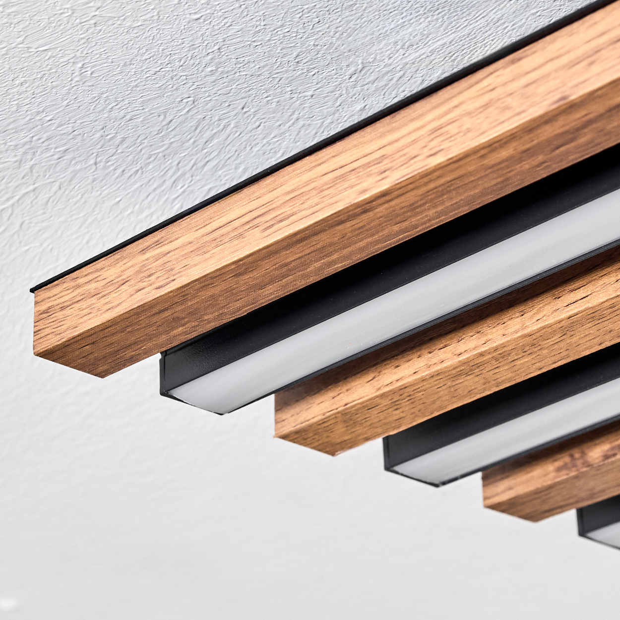 Nahaufnahme einer Decke mit Holzpaneelen. Braune Holzbalken, schwarze Akzente und weiße Lichter sind vor einer strukturierten weißen Decke sichtbar.