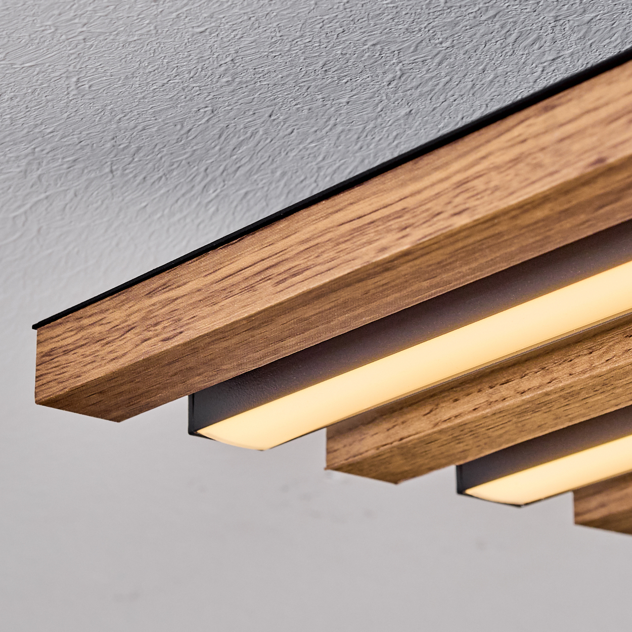 Holzdeckenleuchte mit integrierten Lichtern. Die Leuchte besteht aus Holz und schwarzem Metall. Der Hintergrund ist eine weiße strukturierte Decke.