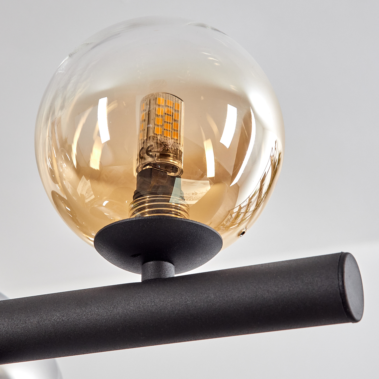 Nahaufnahme einer modernen Leuchte. Sie hat eine runde, bernsteinfarbene Glaskugel mit einer zentralen LED-Glühbirne. Ein schwarzer Metallarm trägt sie.