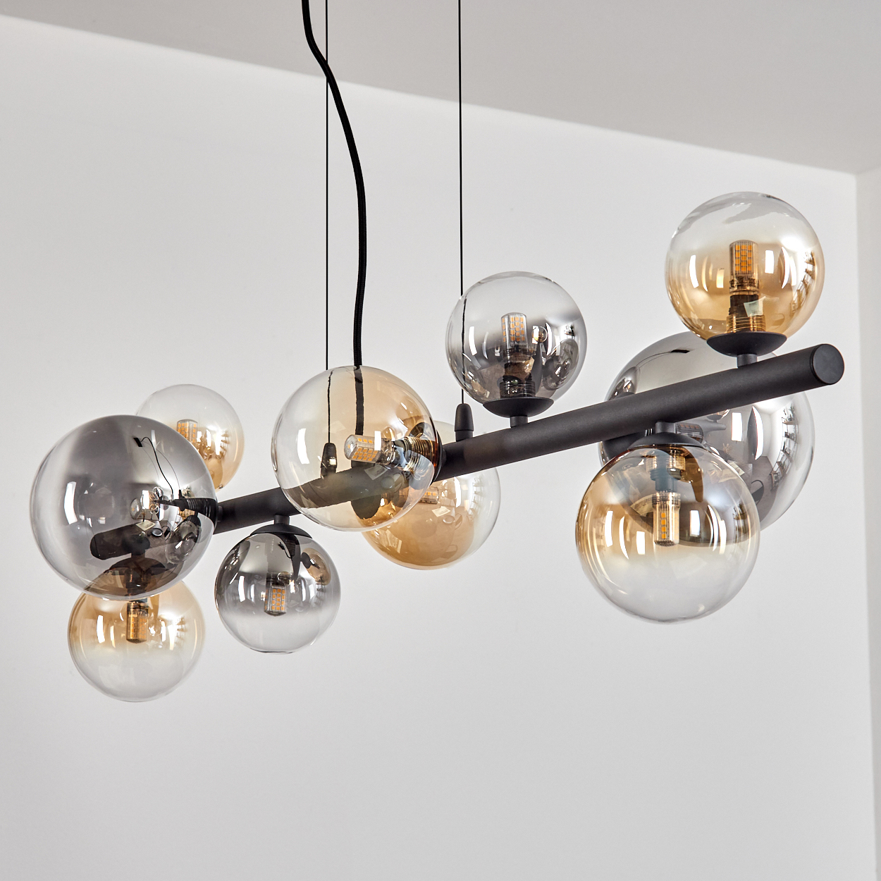 Eine moderne Deckenleuchte mit mehreren kugelförmigen Glasschirmen in Bernstein und Silber, die von der Decke abgehängt sind. Eine schwarze Stange stützt die Lichter.