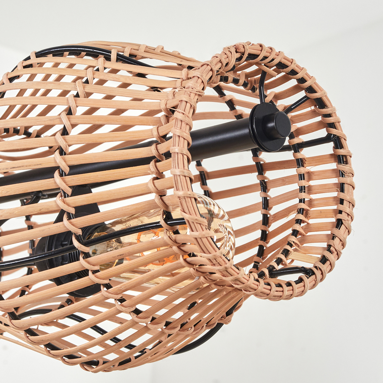 Nahaufnahme einer gewebten Rattanlampe mit schwarzem Metallrahmen. Eine Glühbirne ist im Inneren der Lampe vor weißem Hintergrund zu sehen.