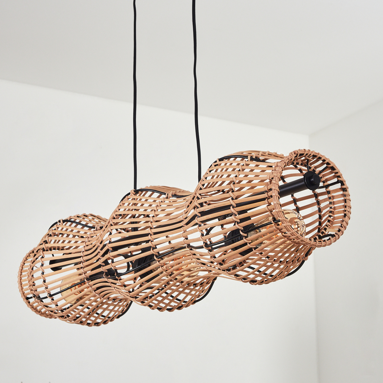 Eine gewebte Rattan-Leuchte mit drei verbundenen Schirmen hängt von der Decke. Schwarze Kabel und Metallstützen sind sichtbar.