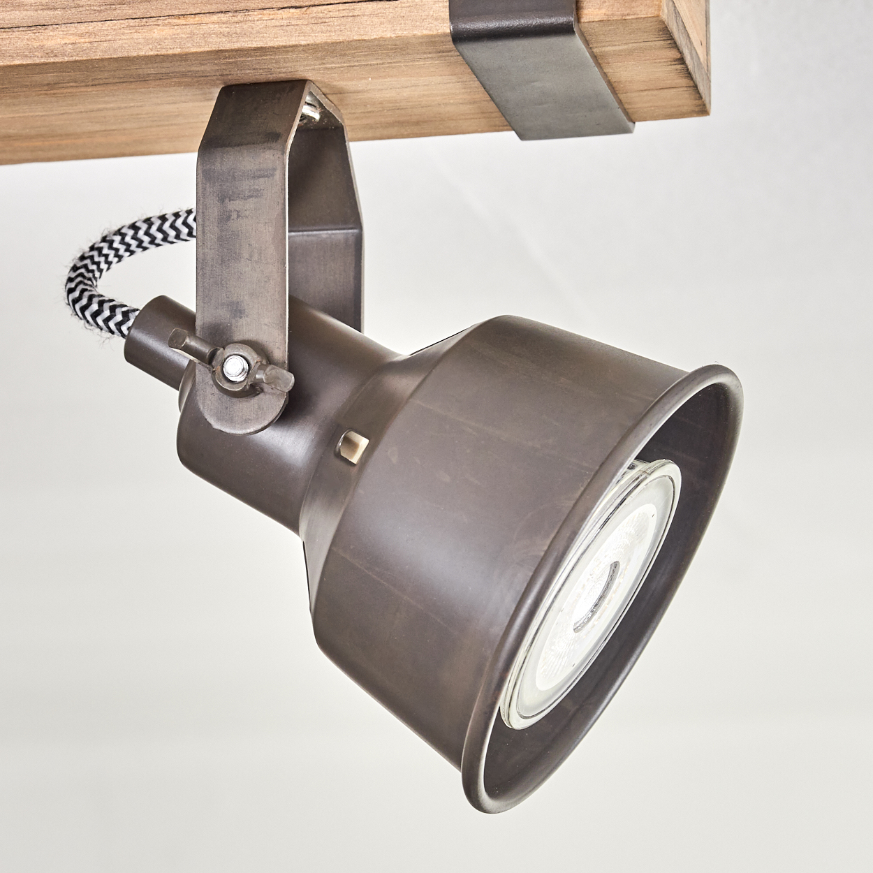 Ein brauner Strahler ist an einem Holzbalken befestigt. Das Licht hat eine runde Glühbirne und ein schwarz-weiß gestreiftes Kabel.