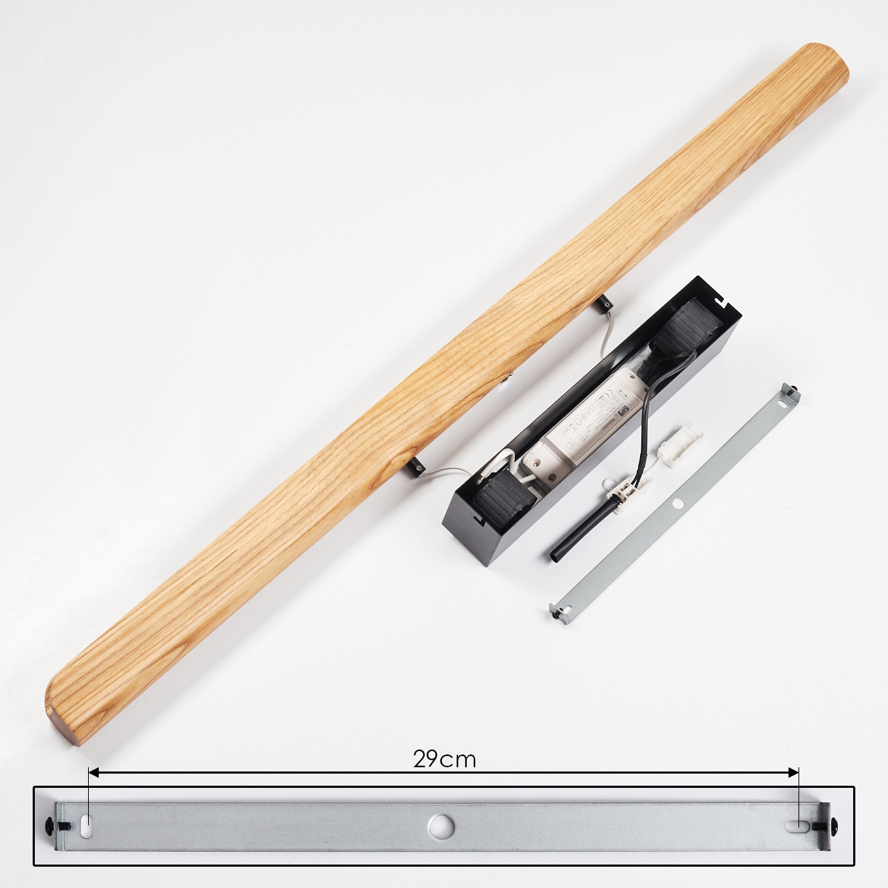 Eine zerlegte Holzleuchte liegt auf einer weißen Oberfläche. Sie enthält einen Holzbalken, eine schwarze elektrische Komponente und eine Metallhalterung.